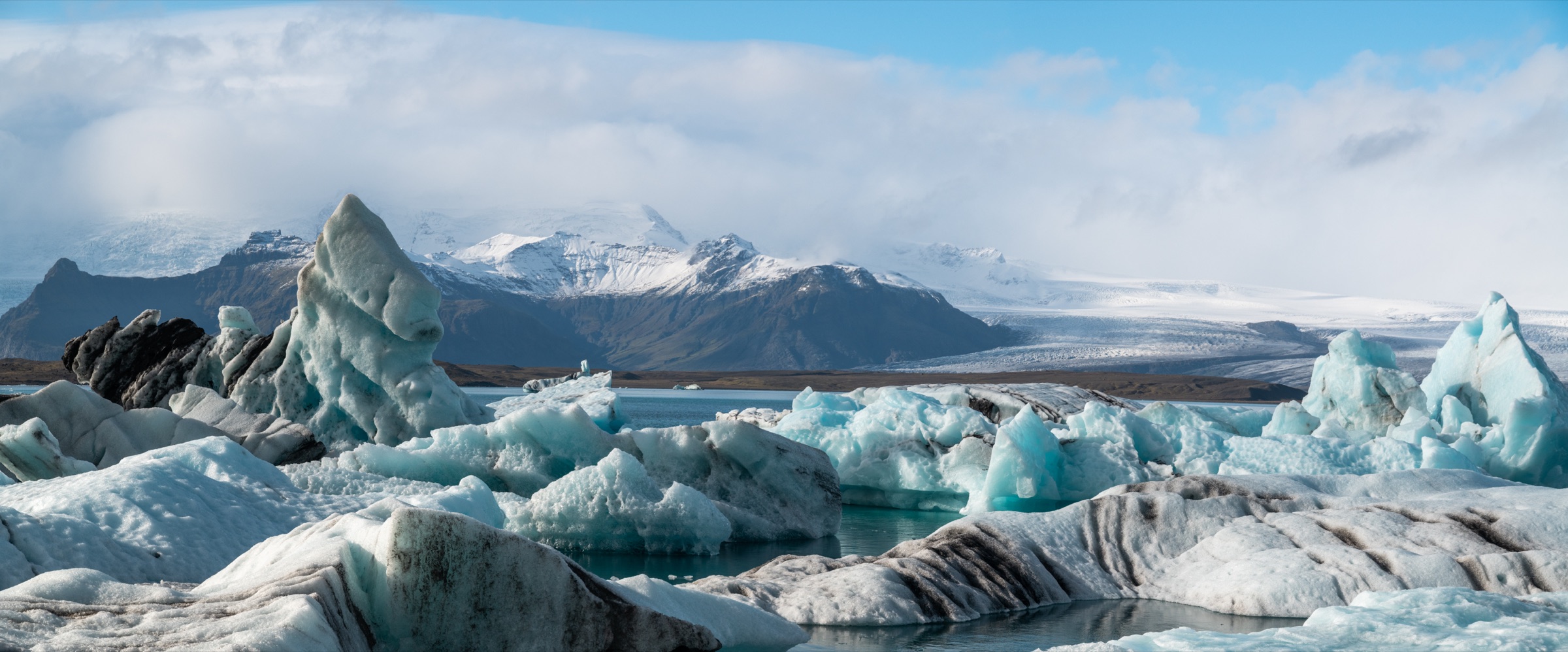 Bright blue glacier icebergs floating on a lagoon below snow-capped mountains